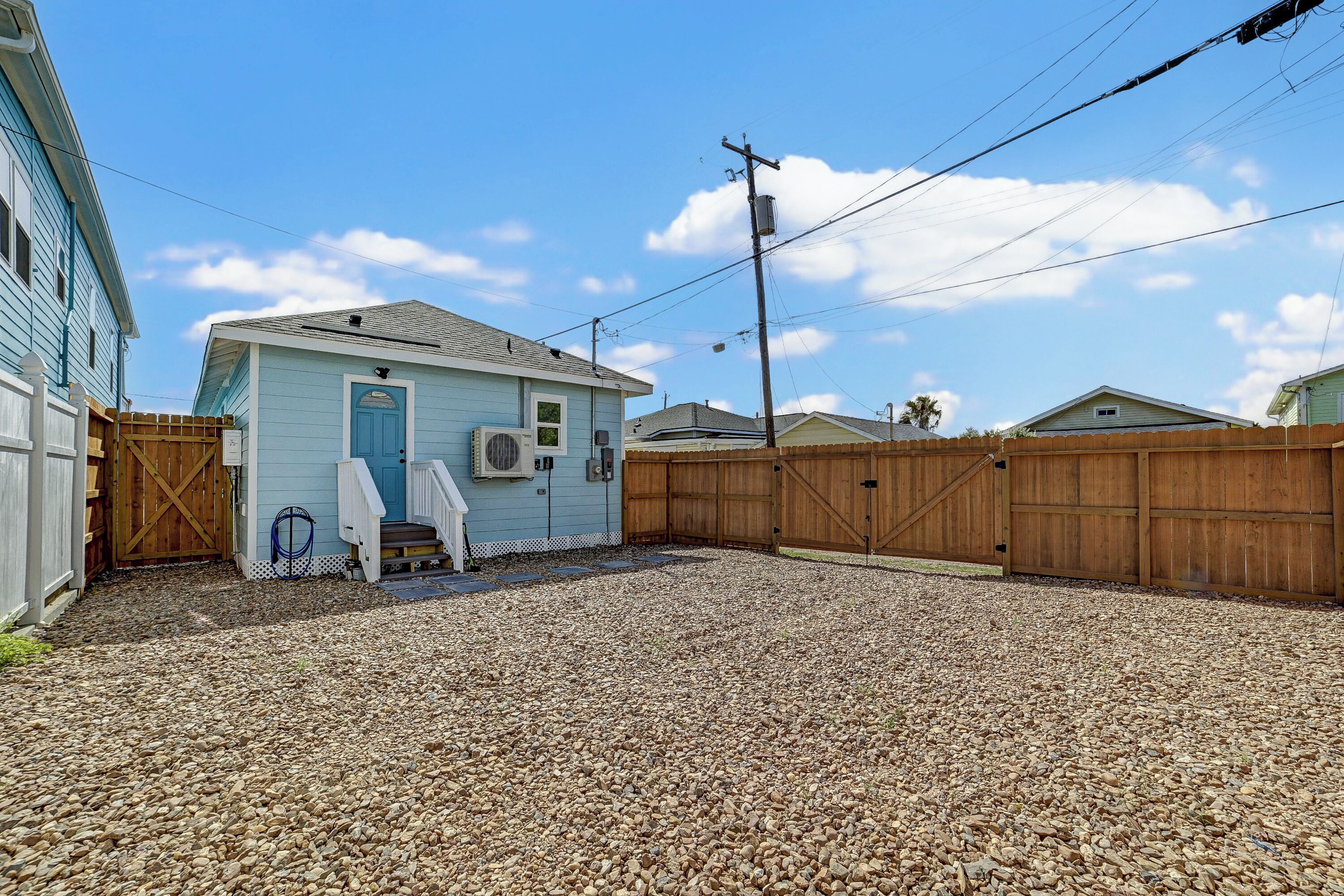 A residential property with a gravel driveway, a wooden fence, and a light blue house with a blue door.