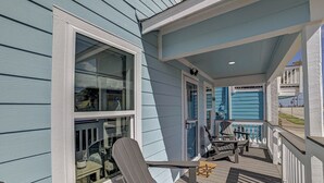 A covered porch with Adirondack chairs, a small table, and a view of the house. - Nautical Nest - 1 block to the Beach, Newly Renovated (Galveston)