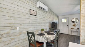 Un coin repas avec un mur en bois, une table blanche recouverte d’une nappe à motifs et des chaises.