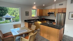 A modern kitchen with wooden cabinets, stainless steel appliances, and a dining area with wicker chairs and a glass table. - Charming 2-bedroom guest house in quiet neighborhood.  

 (Goleta)
