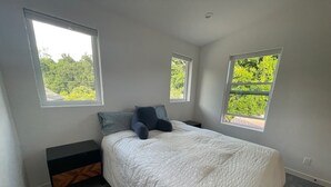 A bedroom with a bed, two windows, a nightstand, and a small wooden bench. - Charming 2-bedroom guest house in quiet neighborhood.  

 (Goleta)