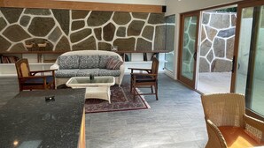 A modern living room with a stone wall, a sofa, two chairs, a coffee table, and a glass door leading outside. - Charming 2-bedroom guest house in quiet neighborhood.  

 (Goleta)