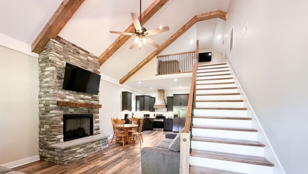 Un salón espacioso con chimenea de piedra, un sofá gris y una escalera de madera que sube a un nivel superior.
