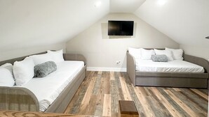 Un dormitorio moderno y luminoso en el ático, con dos camas, suelo de madera y un televisor de pantalla plana montado en la pared.