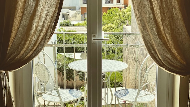 A balcony with white metal chairs and tables, curtains, and a view of buildings and trees. - HABITARE Lecce & Salento (Lecce)