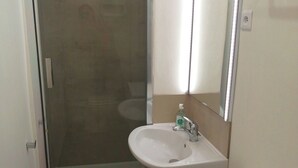 Un baño con cabina de ducha de vidrio, un lavamanos blanco con espejo y una alfombra color beige en el suelo.