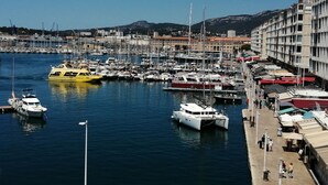 Un puerto deportivo con barcos amarrados, un ferry amarillo y edificios al fondo.