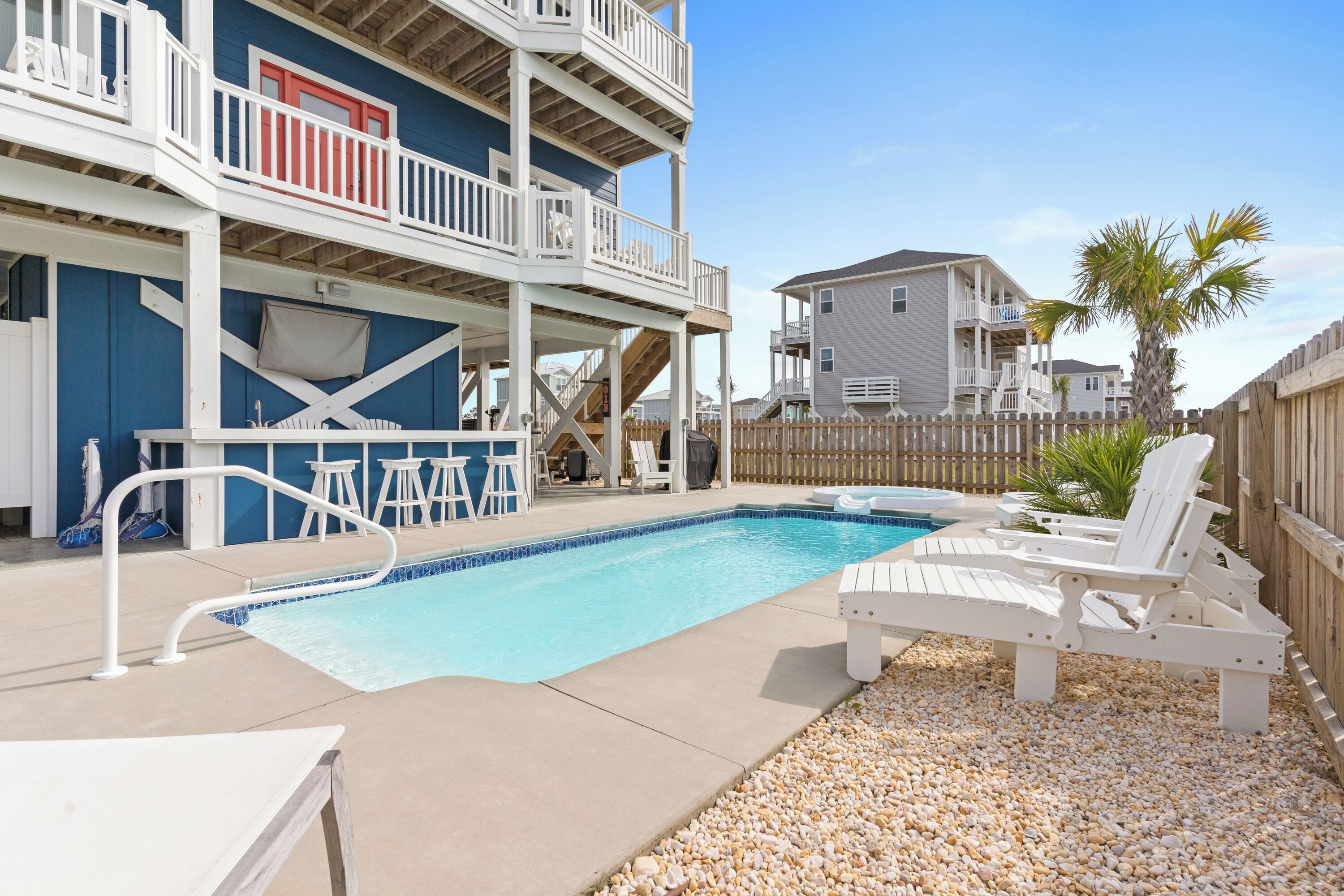 A pool area with a two-story building, a wooden fence, and a palm tree.
