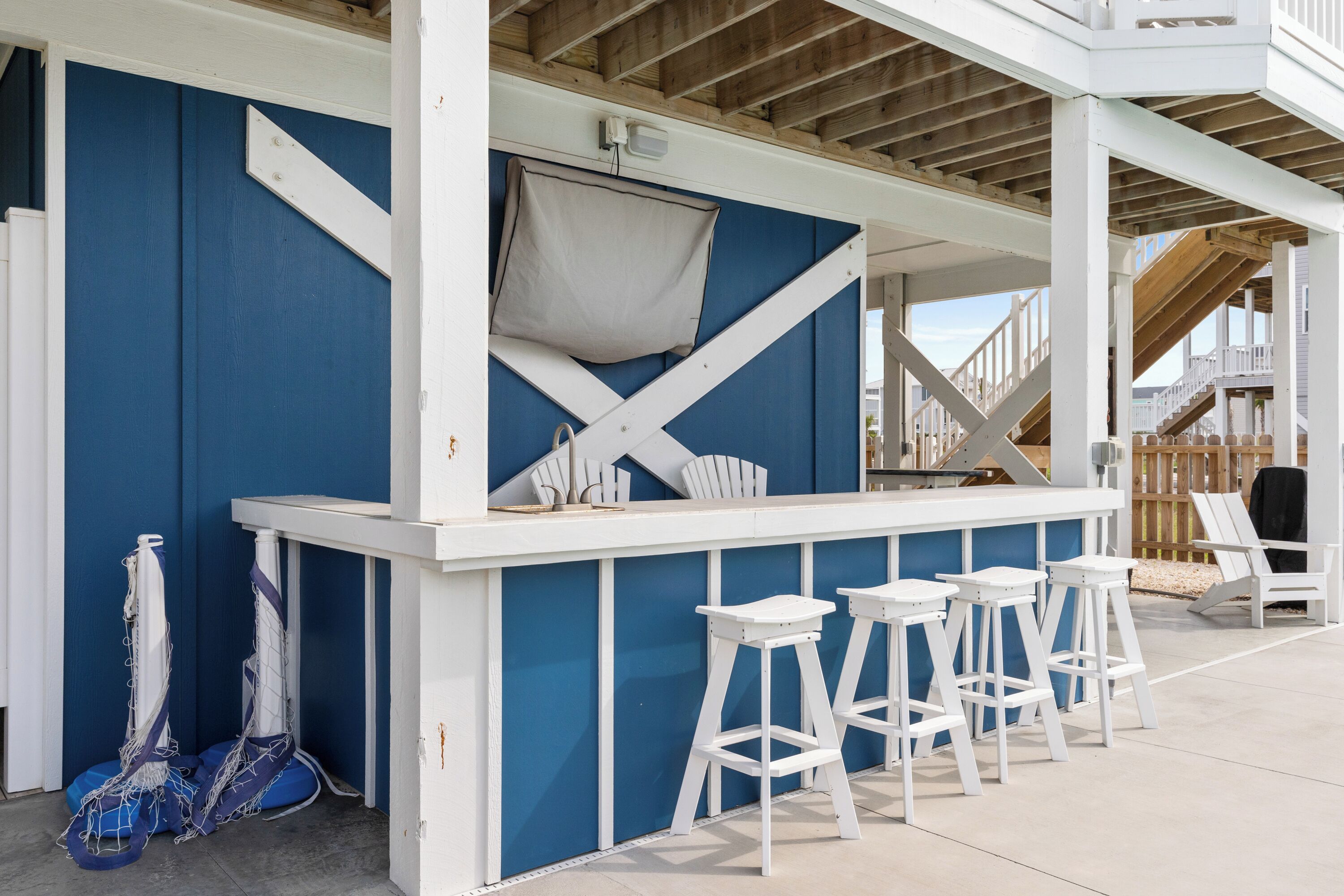A bar area with white bar stools, a blue wall, and a wooden deck.