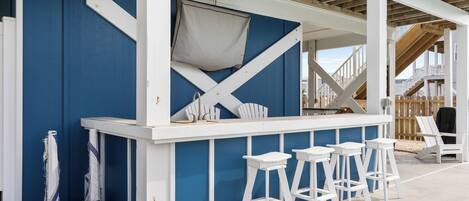 A bar area with white bar stools, a blue wall, and a wooden deck.