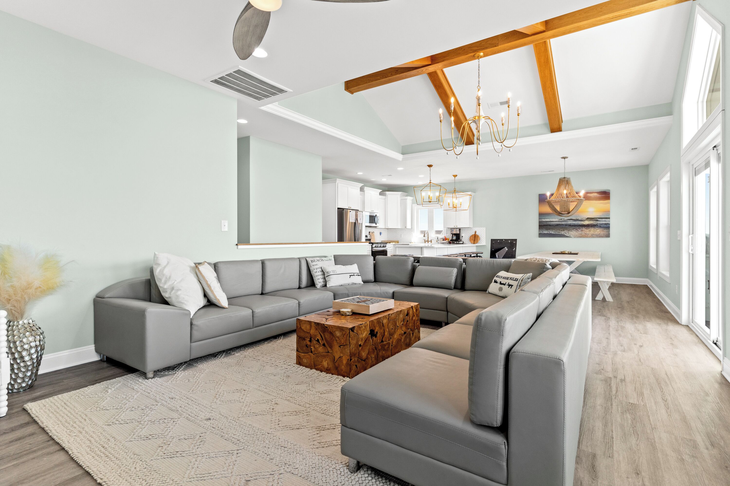 A spacious living room with a large gray sectional sofa, a wooden coffee table, and a modern kitchen in the background.