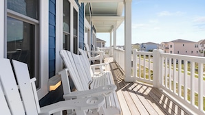 A covered porch with white Adirondack chairs, a white railing, and a view of neighboring houses. - Luxury Ocean View Oasis - Private Pool, Hot Tub, Elevator, 100 Steps to Sand! (Ocean Isle Beach)