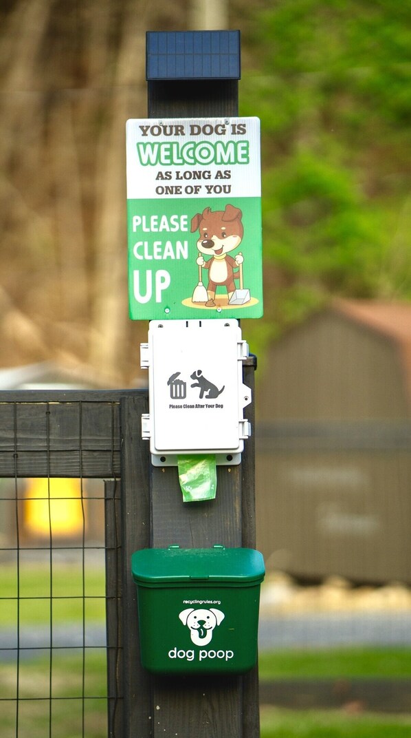 A dog waste station with a sign that reads "YOUR DOG IS WELCOME AS LONG AS ONE OF YOU PLEASE CLEAN UP".