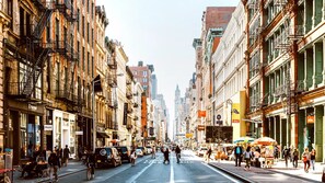 A busy urban street lined with multi-story buildings, some with fire escapes, and pedestrians.