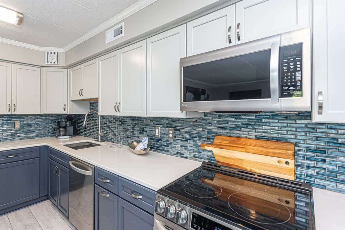 A modern kitchen with white cabinets, a stainless steel microwave, a black stove, and a blue-tiled backsplash.