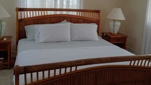 Una cama de madera con ropa de cama blanca, dos mesitas de noche con lámparas y una ventana con cortinas traslúcidas.