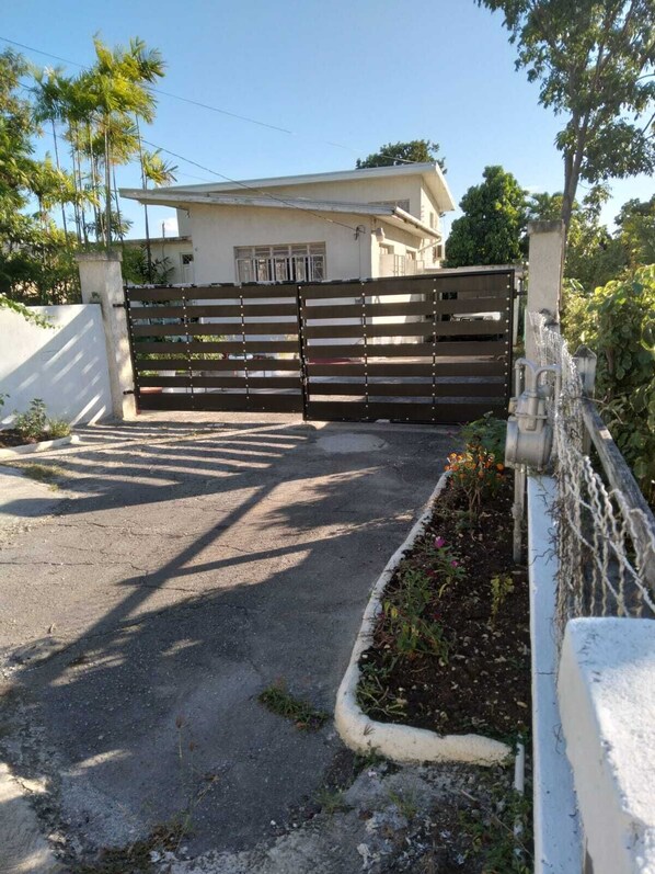 Un camino de entrada cerrado por una reja que lleva a una casa de fachada blanca y un garaje.