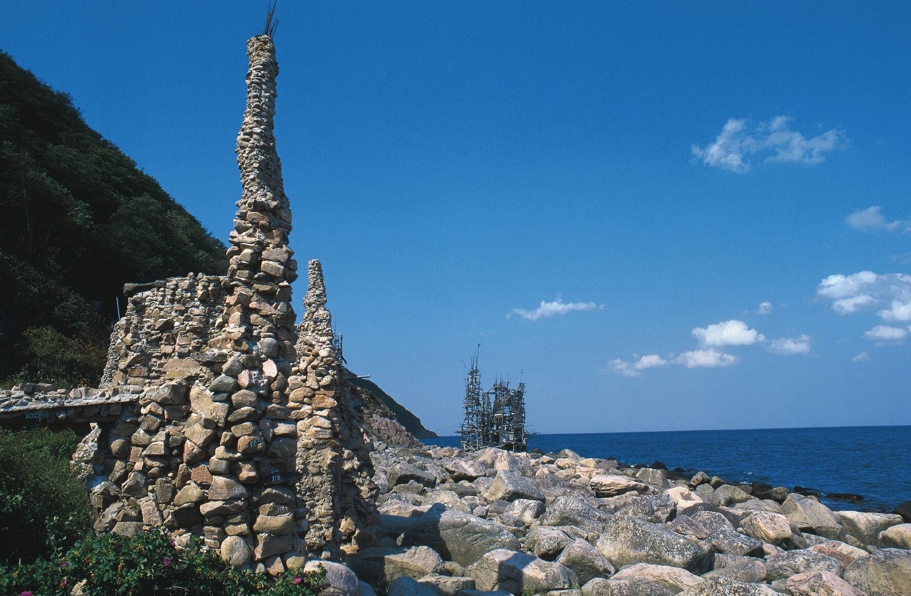 A coastal stone structure with a clear view of the sea and a distant island.