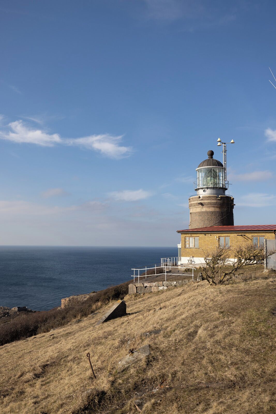 Un faro con techo rojo, ubicado en una colina cubierta de hierba con vista al mar.