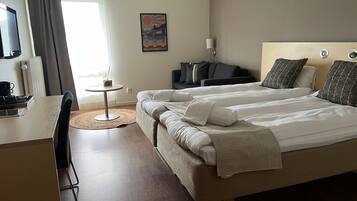 A hotel room with a bed, a desk, a chair, a small table, and a window with curtains.