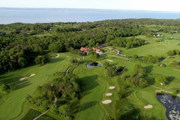 An aerial view of a golf course with multiple bunkers, a pond, and a large body of water in the background. - Visit Örestrand (Strandbaden)