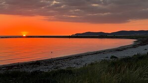 A sunset over a calm body of water with a distant shoreline and hills. - Visit Örestrand (Strandbaden)