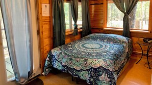Een houten kamer met een bed, gordijnen en een raam met uitzicht op bomen.