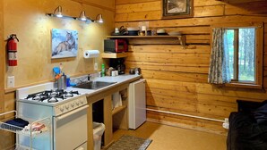 Een gezellig keuken in een blokhut met houten wanden, een gasfornuis, een magnetron en een koelkast.