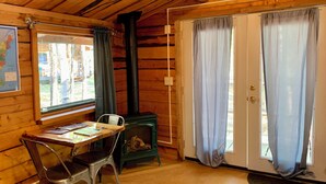 Een houten blokhut van binnen met een tafel, stoelen, een fornuis en een kaart aan de muur.