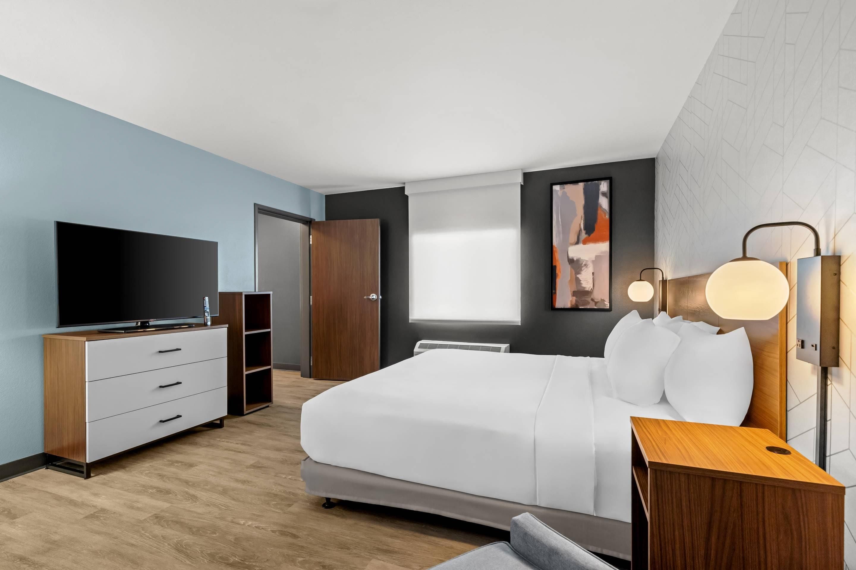Una habitación de hotel moderna con una cama, un televisor, un aparador y una mesita de noche.
