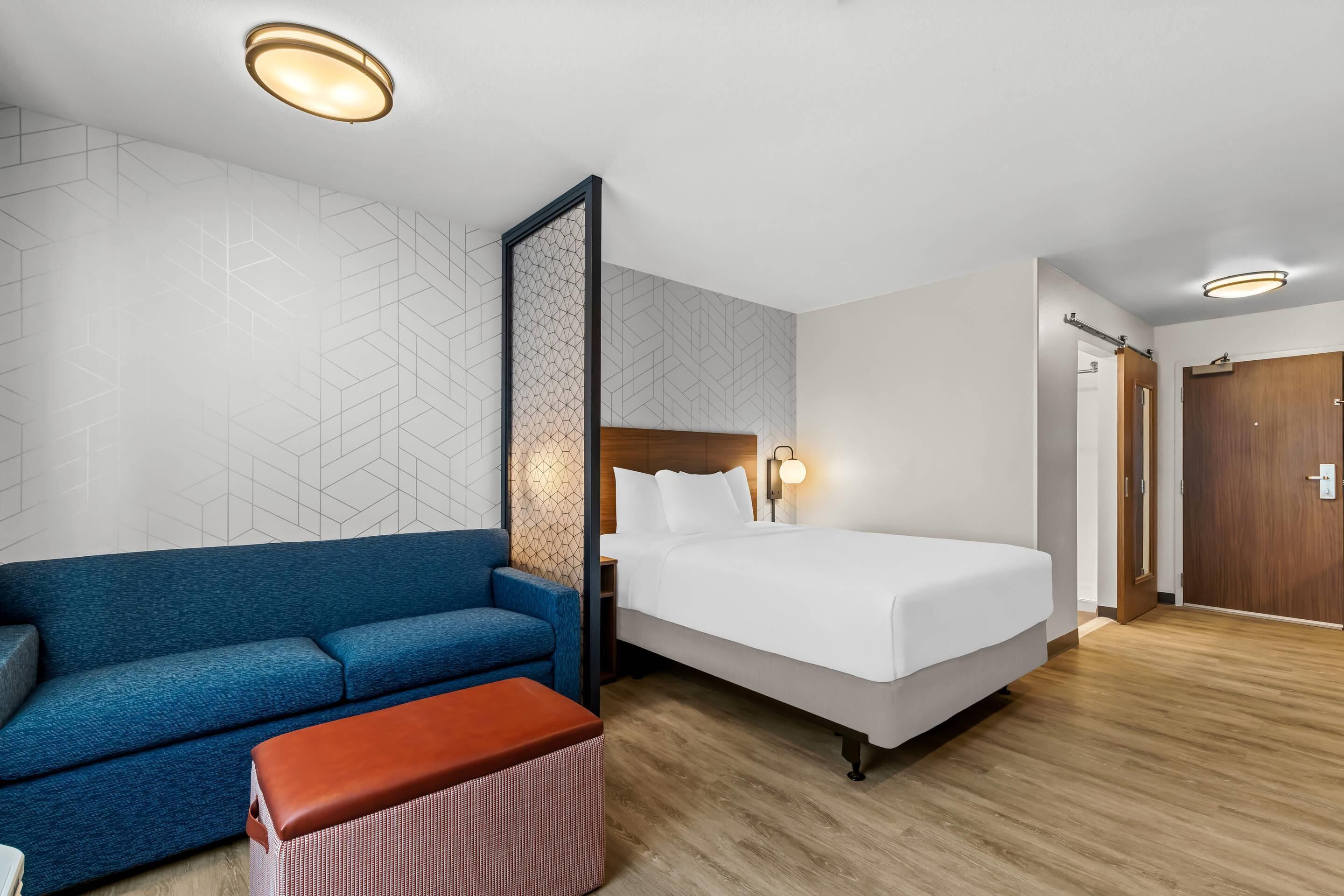 A hotel room with a bed, a blue sofa, a wooden floor, and a wall with a geometric pattern.