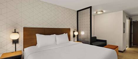 Una habitación de hotel moderna con una cama grande, dos mesitas de noche con lámparas, un pequeño sofá y una pared con estampado geométrico.