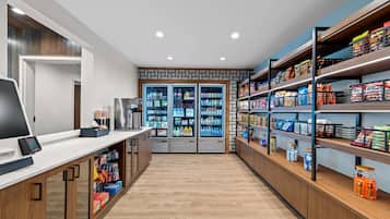 A modern retail space with a checkout counter, refrigerated beverage display, and shelves stocked with snacks and beverages.