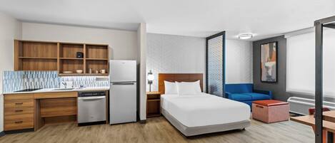 A hotel room with a kitchenette, a bed, a seating area, and a large window.