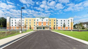 A multi-story hotel with a central entrance, surrounded by a parking lot and greenery. - Woodspring Suites Pensacola West (Pensacola)