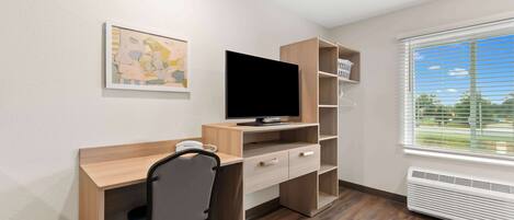 A modern room with a wooden desk, a chair, a flat-screen TV, a bookshelf, and a window with blinds.