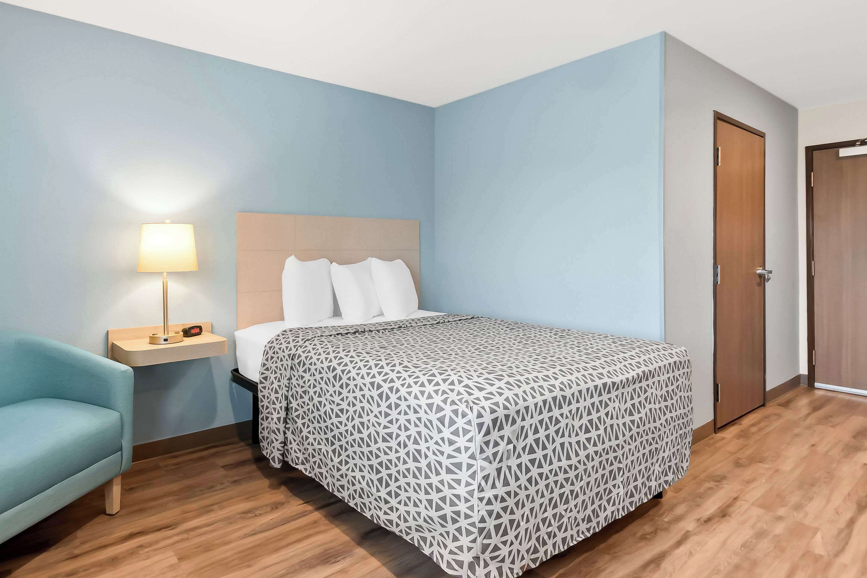 Un dormitorio con cama, mesita de noche, lámpara, silla y puerta.