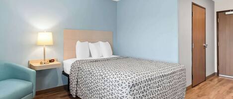 Un dormitorio con cama, mesita de noche, lámpara, silla y puerta.
