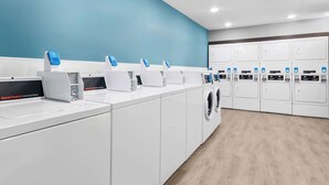A modern laundry facility with multiple washing machines and dryers, a blue wall, and a clean, organized layout. - Woodspring Suites Pensacola West (Pensacola)