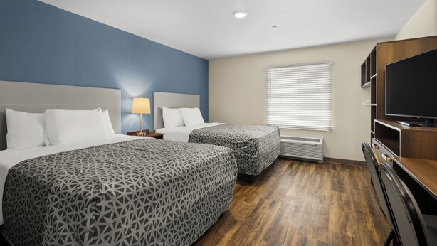 A hotel room with two beds, a TV, and a desk. - Woodspring Suites Pensacola West (Pensacola)