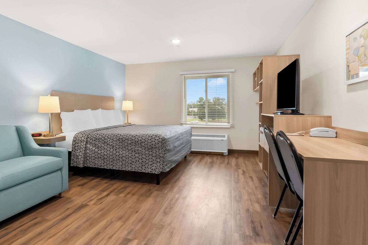 A hotel room with a bed, a desk, a chair, a TV, and a window.
