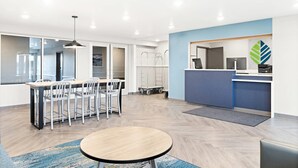 A modern reception area with a blue accent wall, a reception desk, and a waiting area with a round table and chairs. - Woodspring Suites Billings (Billings)