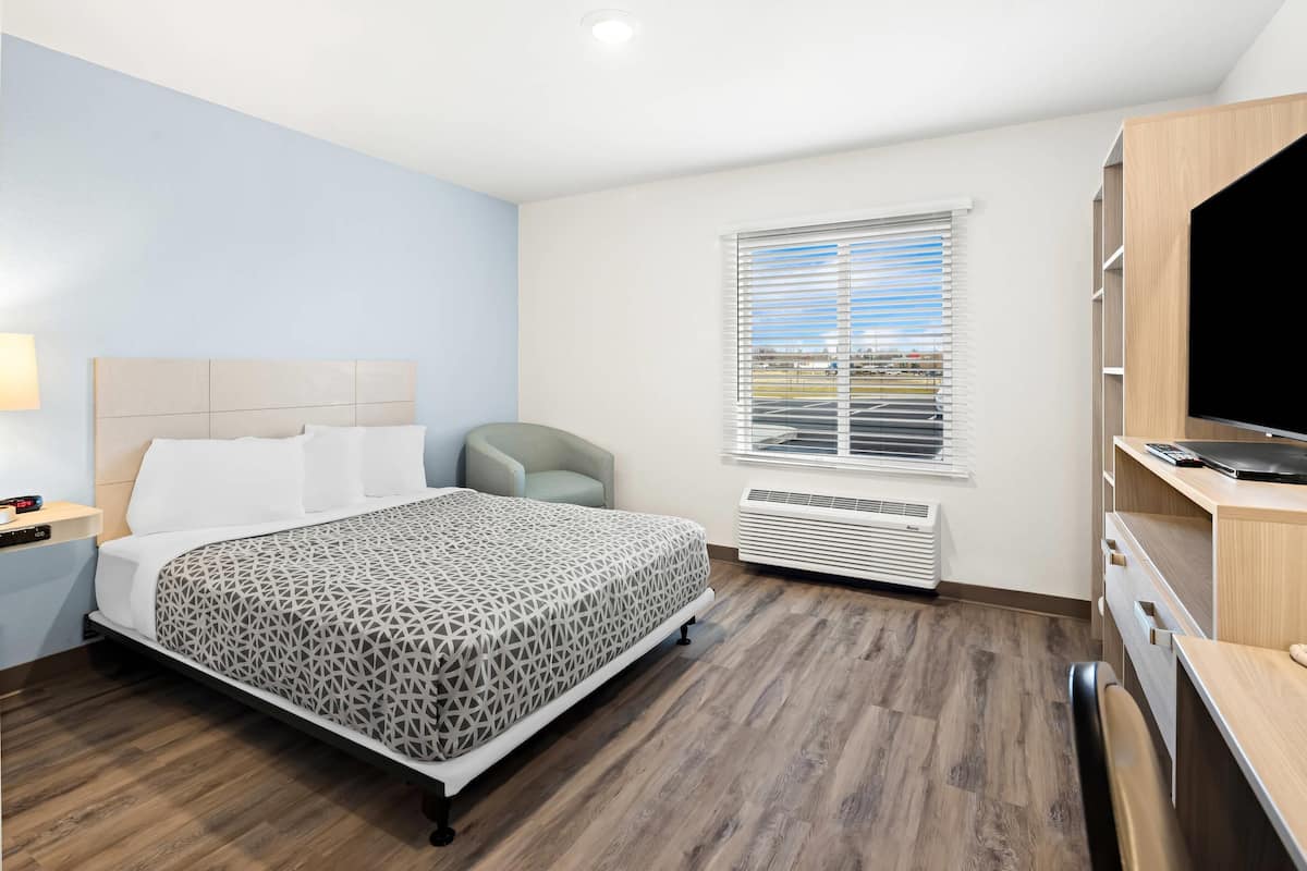 Une chambre d’hôtel équipée d’un lit, d’un bureau, d’une chaise, d’une télévision et d’une fenêtre avec des stores.