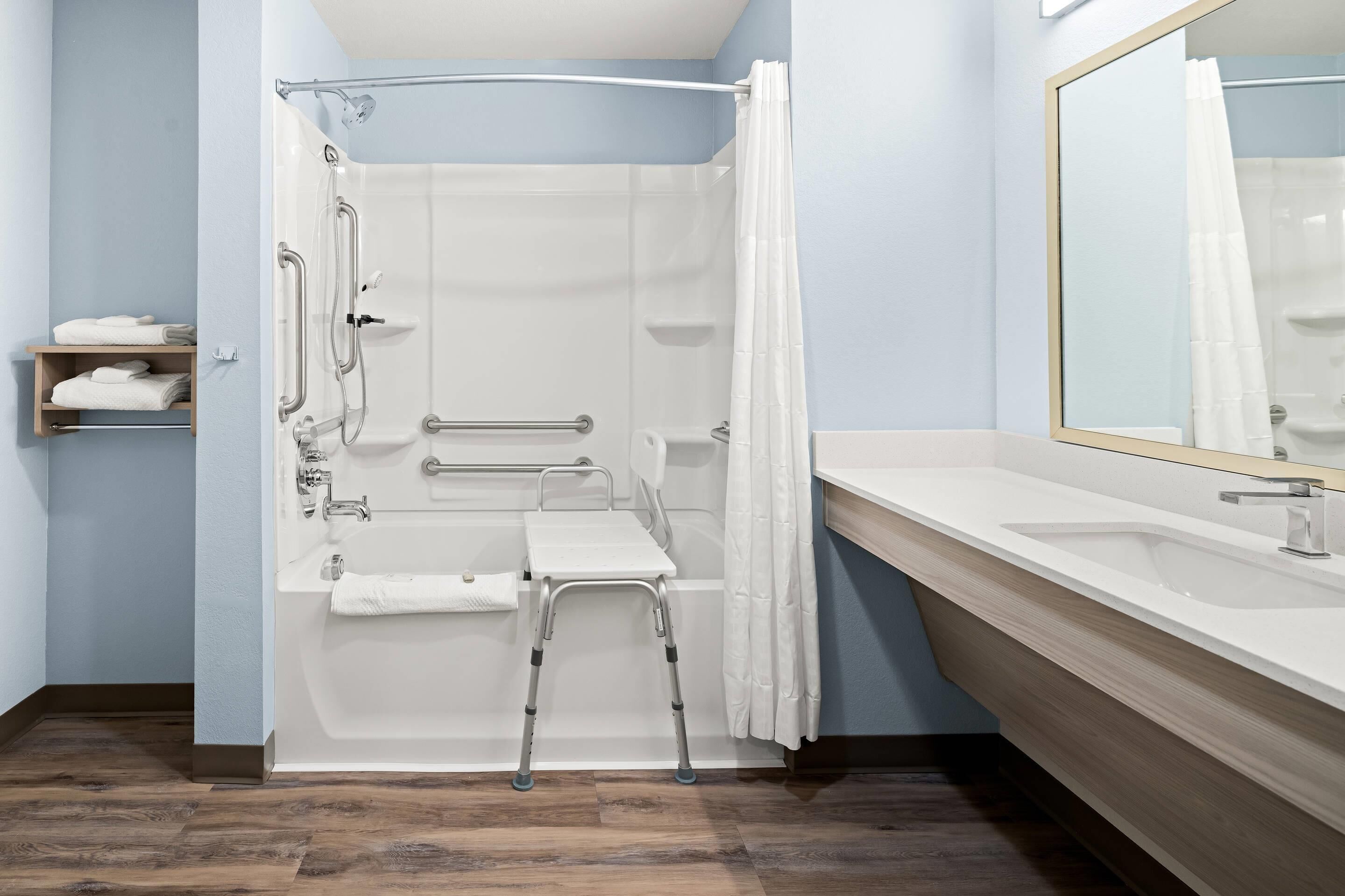 A modern bathroom with a walk-in shower, grab bars, a white towel rack, and a large mirror.