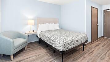 Una habitación de hotel con cama, mesita de noche, lámpara, silla y piso de madera.