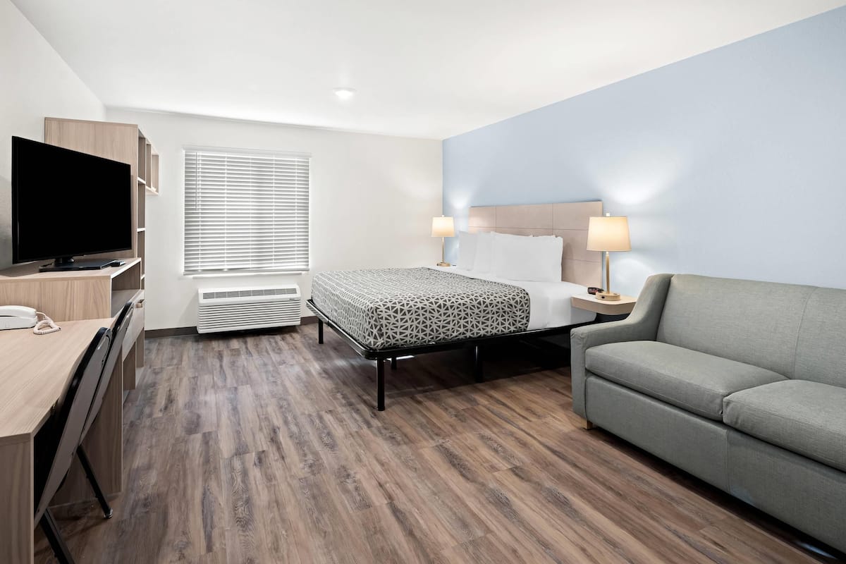 Une chambre d’hôtel avec un lit, un canapé, un bureau avec une télévision et une fenêtre avec des stores.