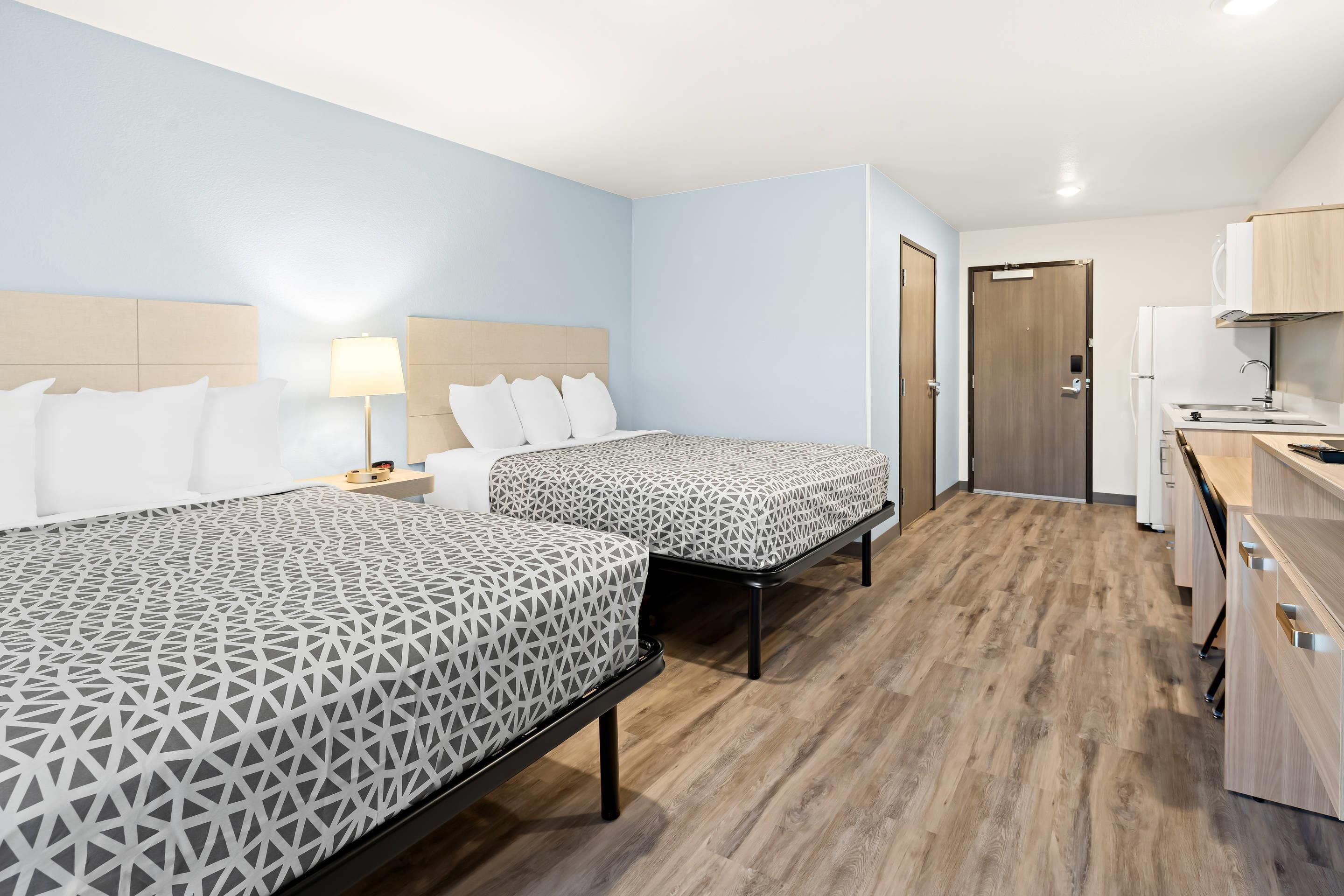 A hotel room with two beds, a kitchenette, and a bathroom.