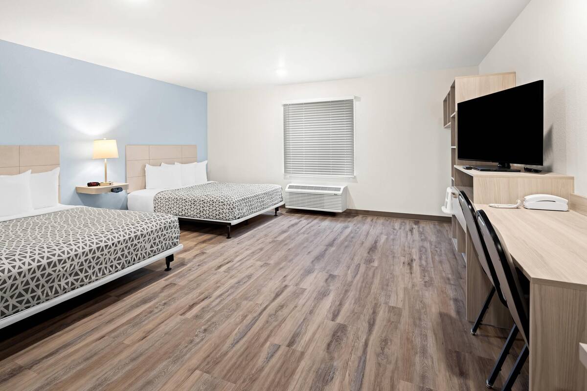 Une chambre d’hôtel avec deux lits, un bureau, une télévision et une fenêtre avec des stores.