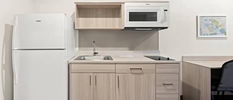 Cocina compacta con refrigerador, microondas, pileta y alacenas de madera.