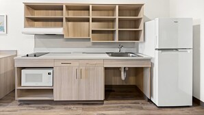 A modern kitchen with wooden cabinets, a built-in microwave, a sink, and a white refrigerator. - Woodspring Suites Billings (Billings)
